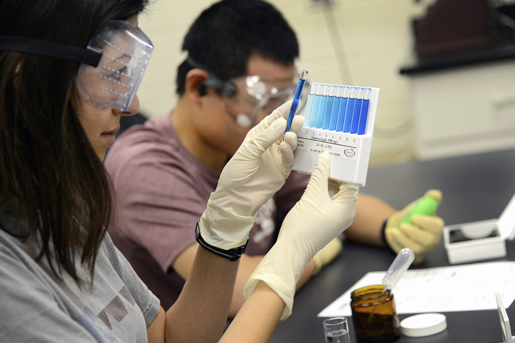 Student holding a ph scale while using white gloves and lab goggles.