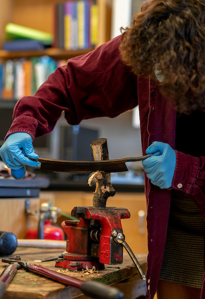 Man cutting some wood while wearing blue gloves in a classroom setting.