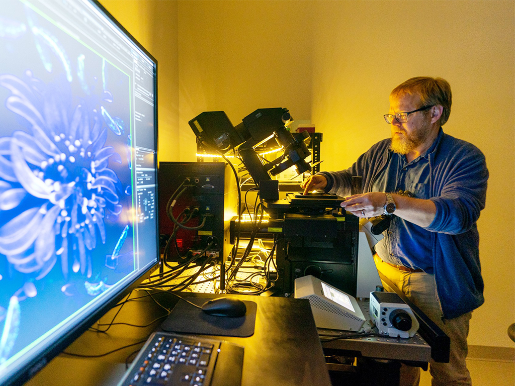 Man adjusting a machine while the screen next him shows a microscopic close up.