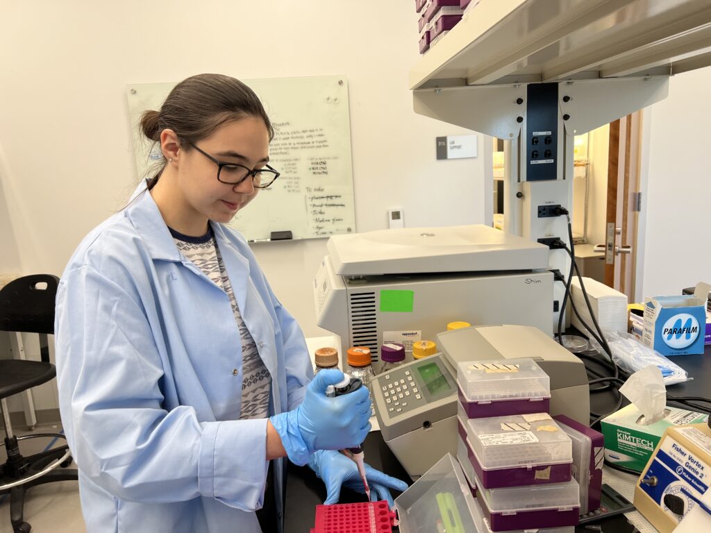 A woman in a lab coat is focused on her work while using a computer in a laboratory setting.