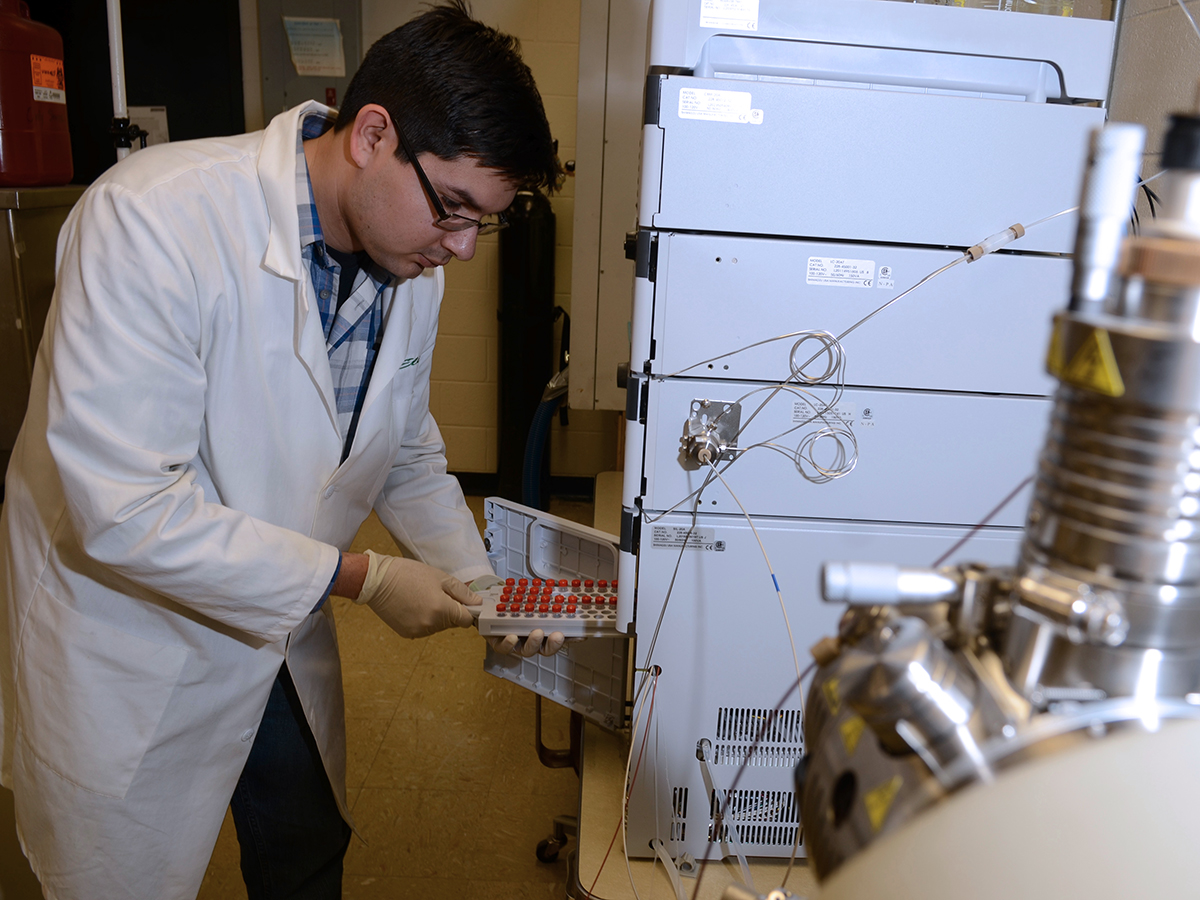 A guy in a lab looking at different samples using white gloves and a white lab coat.