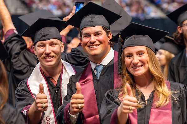 Students at graduation wearing cap and gown showing off their Aggie rings.